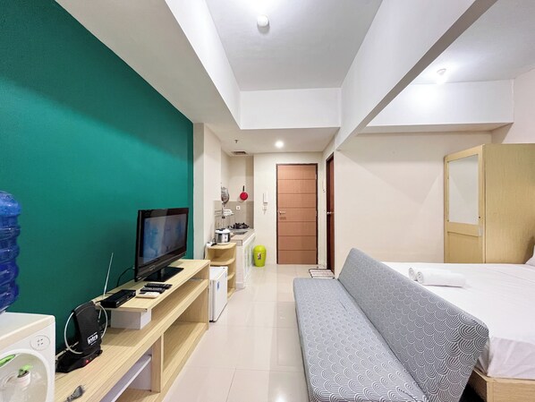 A modern hotel room with a television, a desk with a computer, a sofa, and a bed.