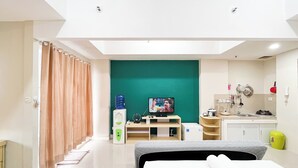 A modern hotel room with a bed, a television, a small kitchenette, and a bathroom.