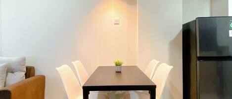 Un espacio habitable funcional con una mesa de comedor, sillas blancas, una pequeña planta en maceta, un sofá marrón y un refrigerador negro.