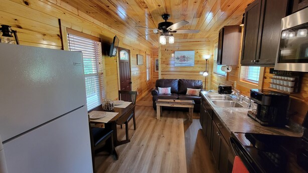 Interior acogedor de una cabaña con detalles de madera, un comedor, un sofá, una cafetera y un refrigerador.