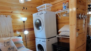 Una habitación acogedora con cama, lavadora, ventilador de techo y cesto de ropa.