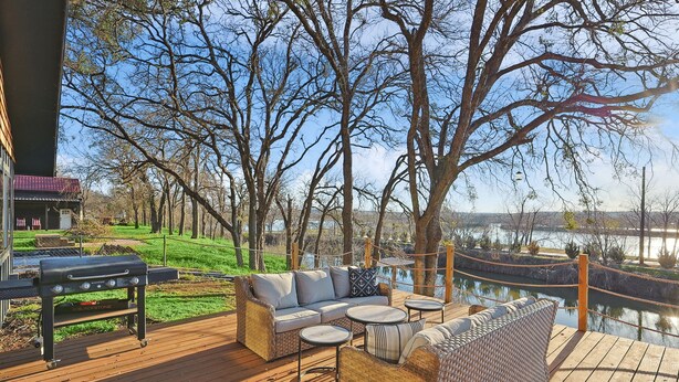 Una terraza con mobiliario de mimbre, una parrilla y vistas a un lago.