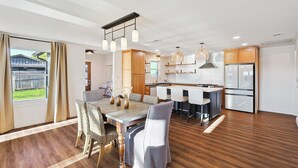 Una cocina moderna con armarios de madera, un refrigerador de acero inoxidable y una zona de comedor con una mesa y sillas de madera.