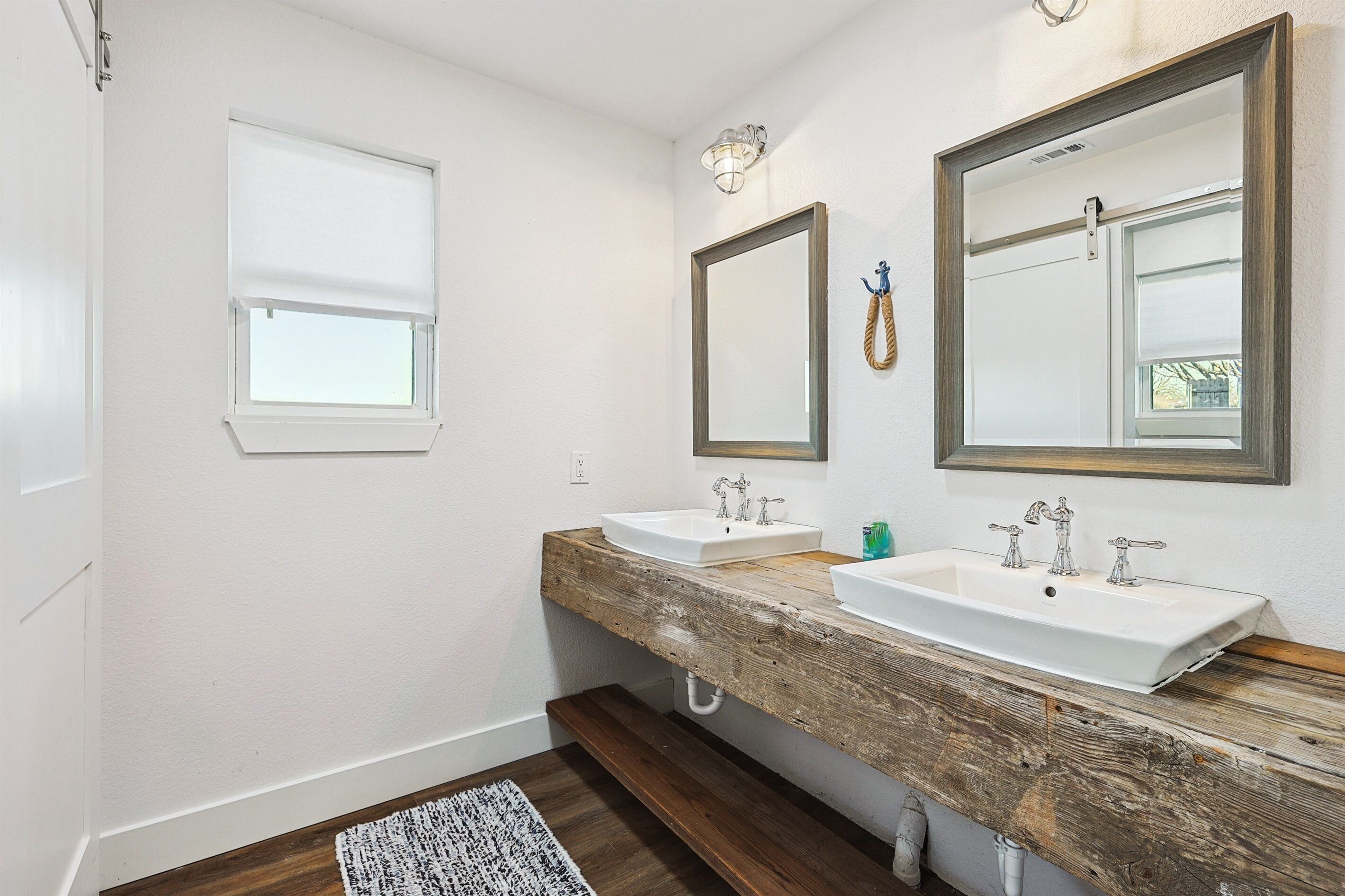 Un baño con dos lavamanos, tocador de madera, paredes blancas y una ventana con persianas.