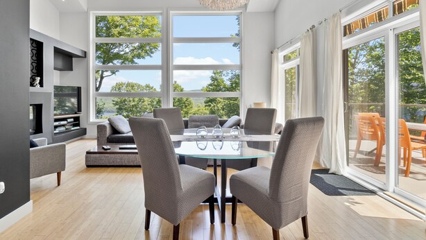 A modern living room with a glass-top dining table, grey upholstered chairs, a sofa, and a television on a black stand.