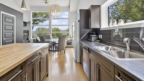 A modern kitchen with a wooden countertop, stainless steel appliances, and a large window offering a view of trees.