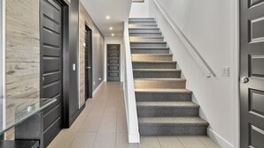 A modern interior with a staircase, dark wooden doors, and a light-colored hallway.