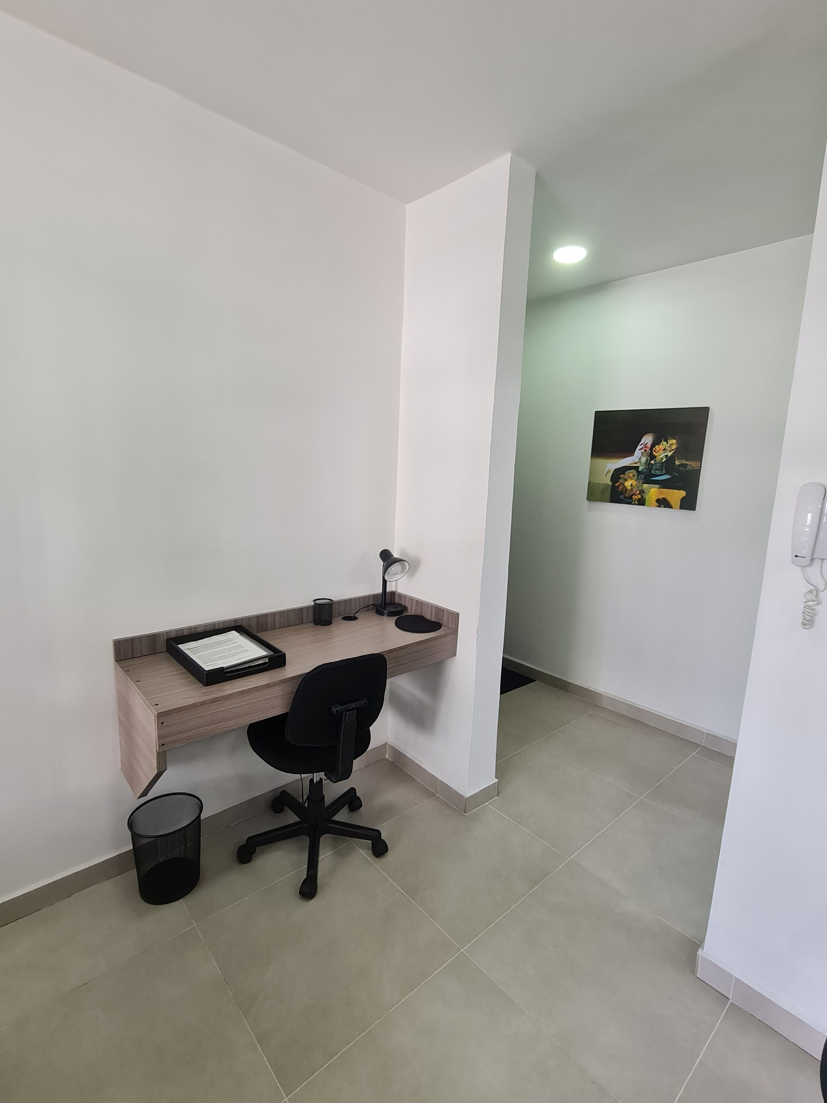 Une petite pièce propre, équipée d’un bureau, d’une chaise et d’une poubelle.