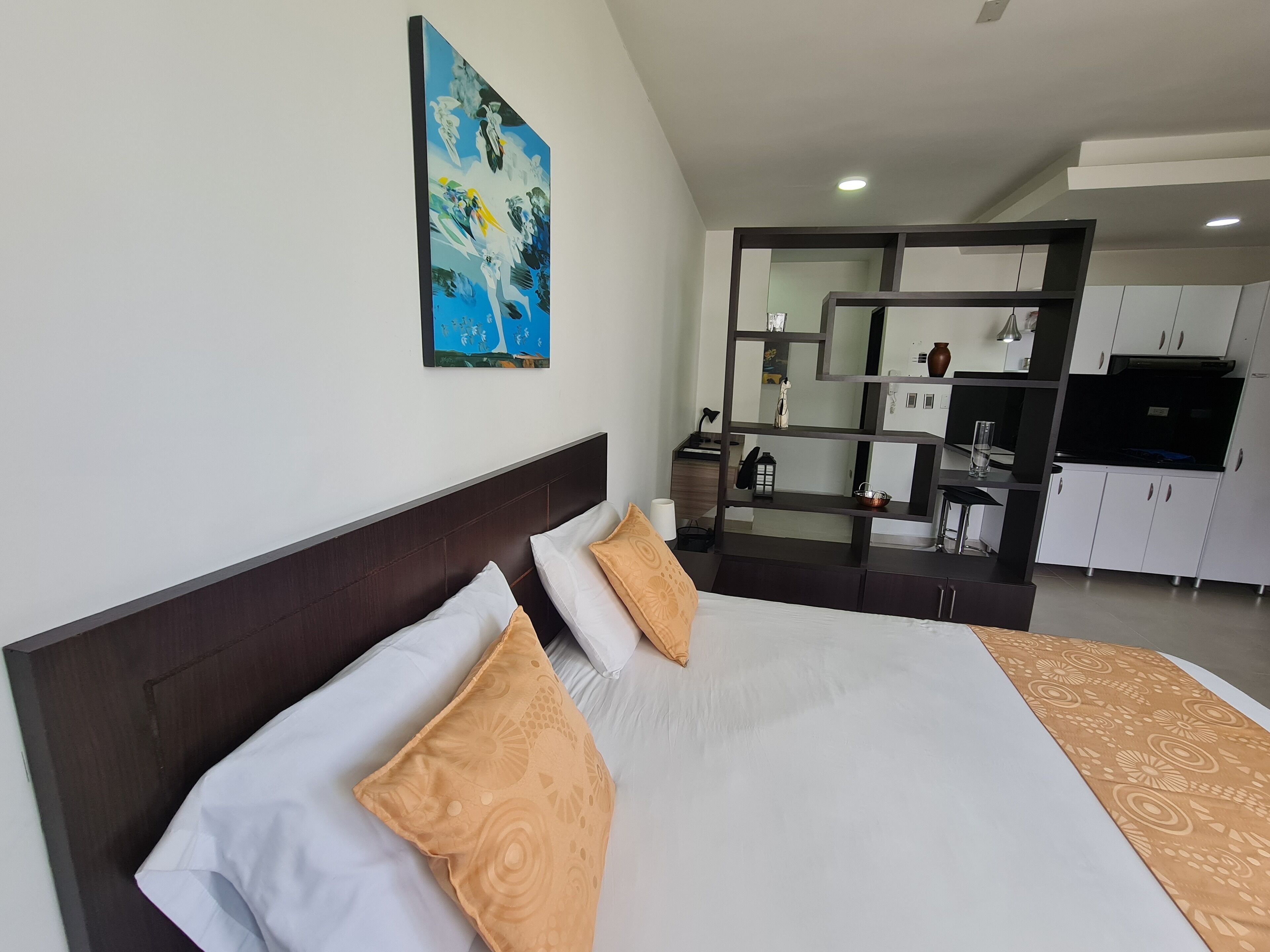Ett modernt hotellrum med en stor säng, en tavla på väggen och ett köksutrymme som syns genom en glasvägg.
