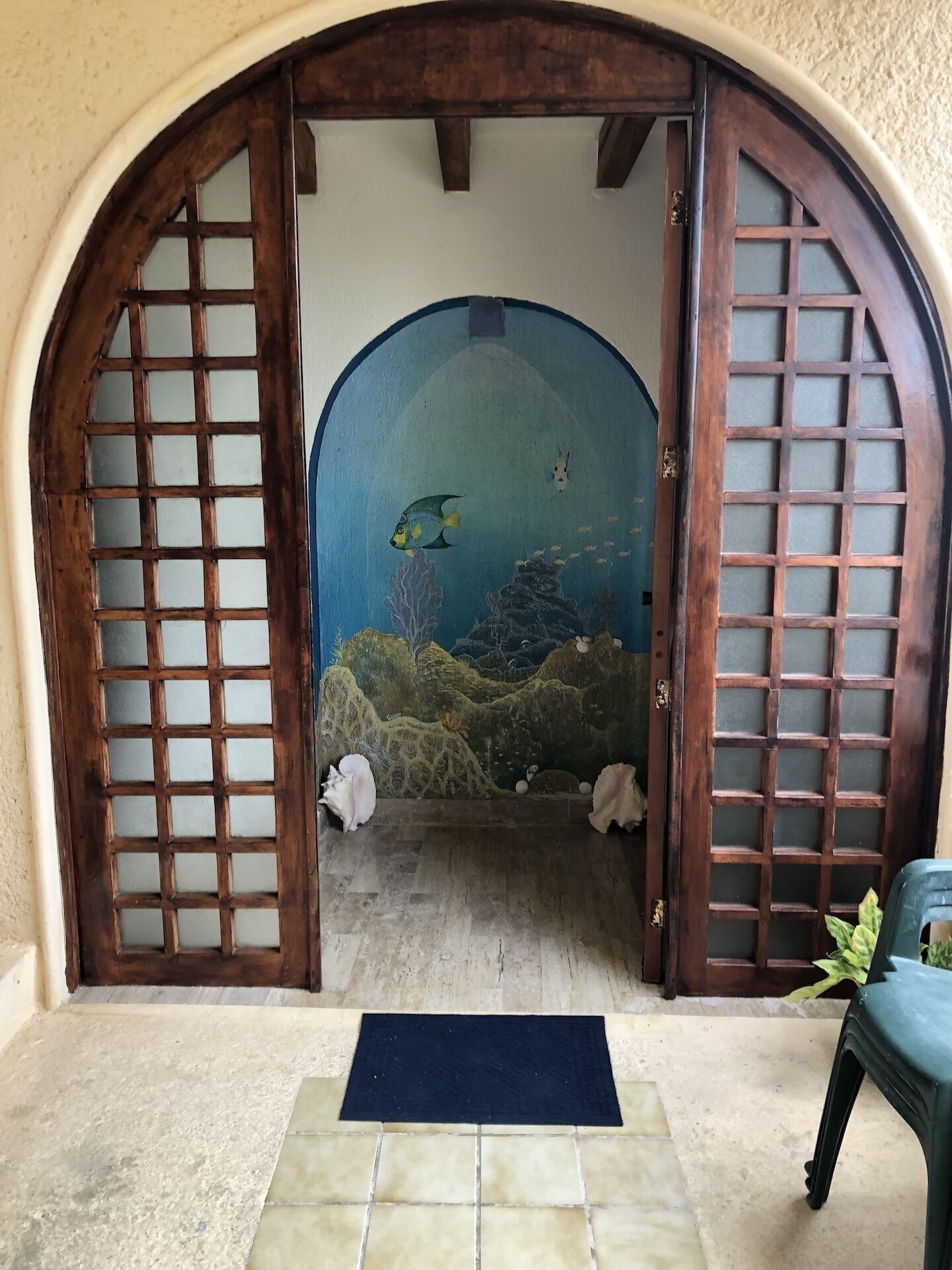 Une pièce dont le sol est recouvert de carreaux, avec un tapis bleu à l’entrée et une fresque représentant une scène sous-marine.