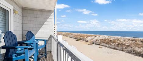 Un balcon avec des fauteuils Adirondack donnant sur une plage bordée de dunes et sur l’océan.