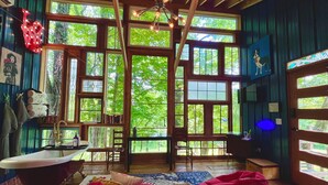 A room with large windows, a bathtub, and a bed with multiple quilts. - Wall of Windows Treehouse-Romantic Woodland Retreat-Escape (Doyle)