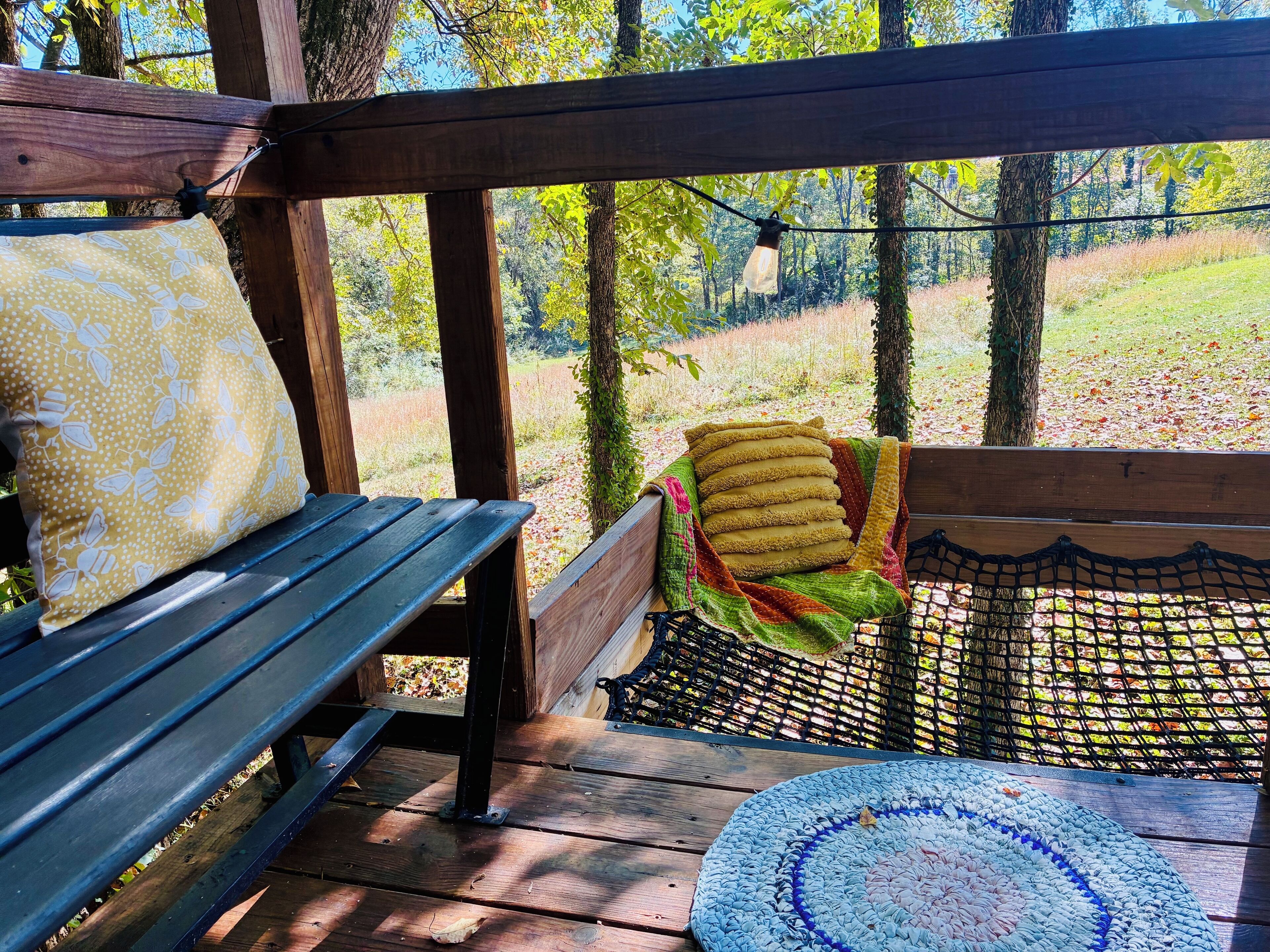 Une terrasse en bois avec un banc et une table, entourée d’arbres et d’une pelouse.