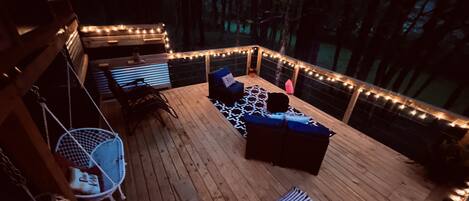 Une terrasse en bois avec des sièges d’extérieur, des guirlandes lumineuses et un fauteuil suspendu.