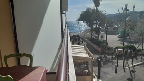 A balcony with a table and chairs, overlooking a street with a carousel and palm trees. - 1 Bedroom Apartment in Cassis (Cassis)