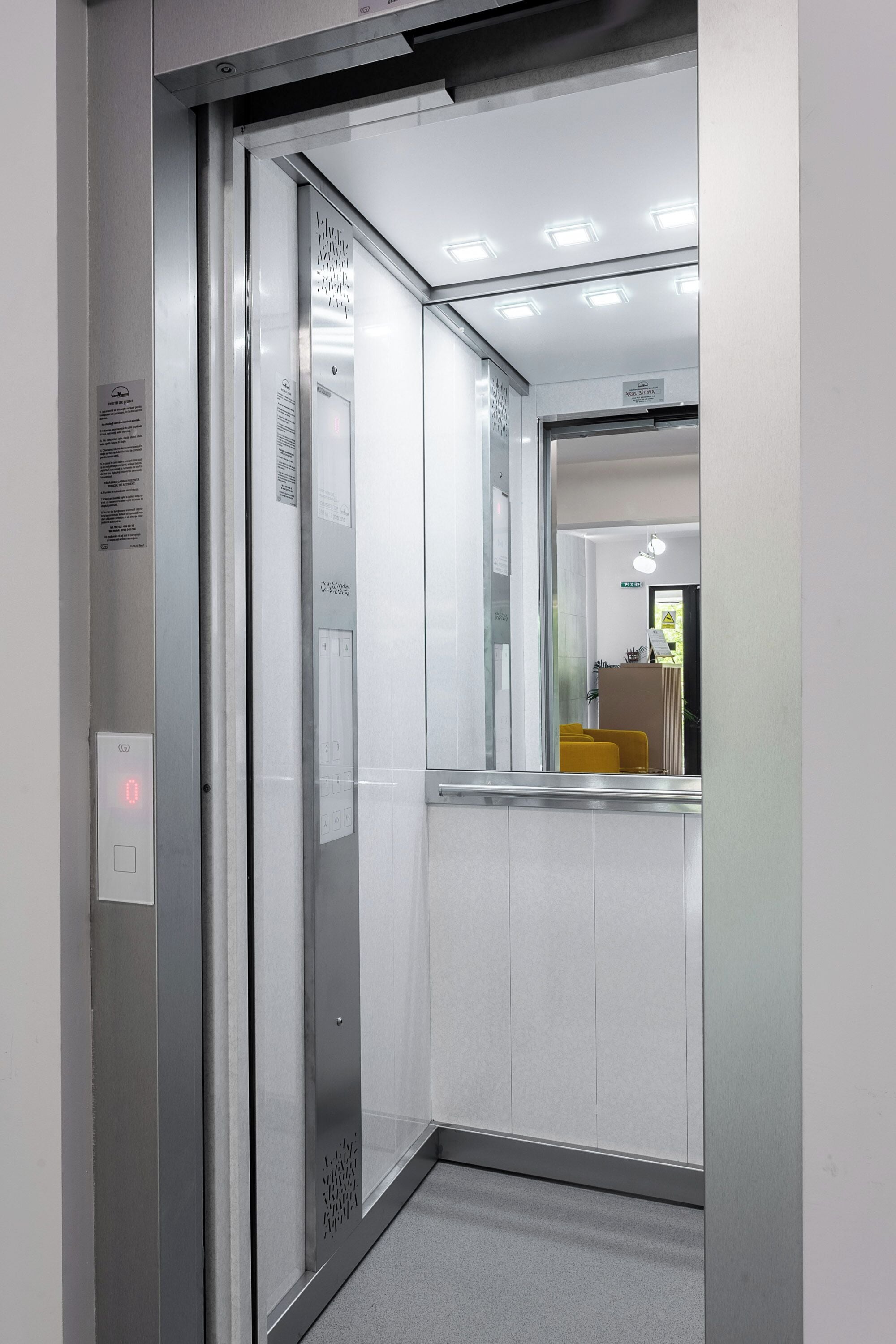 An elevator with a digital display, glass doors, and a ceiling light.