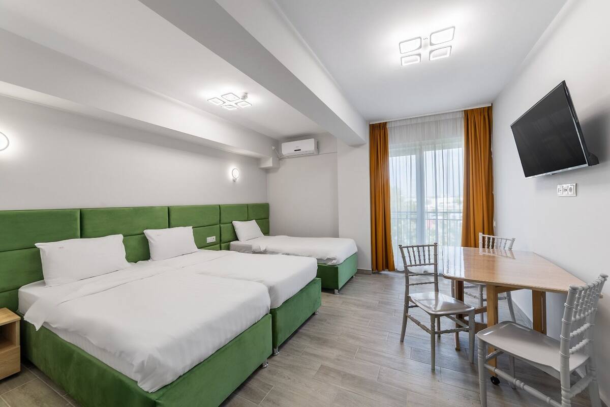Une chambre d’hôtel avec deux lits, une table à manger, des chaises, un téléviseur et une fenêtre avec des rideaux.