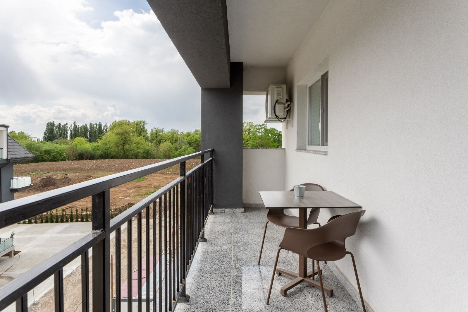 Een balkon met een tafel en stoelen, een hekwerk en uitzicht op een aangelegde tuin.