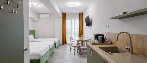 Ein kleines Hotelzimmer mit zwei Einzelbetten, einer Küchenzeile, einer Essecke und einem an der Wand befestigten Fernseher.