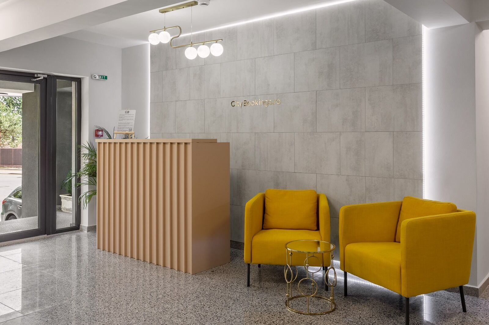 Un área de recepción con diseño moderno, que cuenta con un mostrador de madera, dos sillones amarillos y una pequeña mesa.