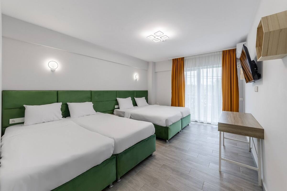 Une chambre d’hôtel avec deux lits simples, un petit bureau et un téléviseur fixé au mur.