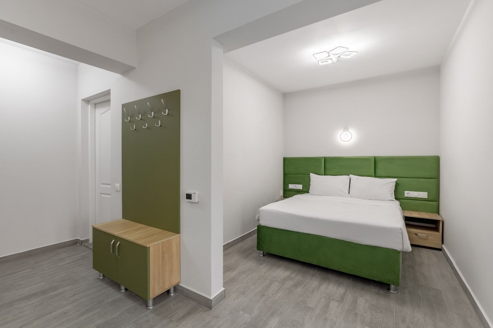 A modern bedroom with a green upholstered bed, a wooden bench, a wardrobe, and a bedside table.