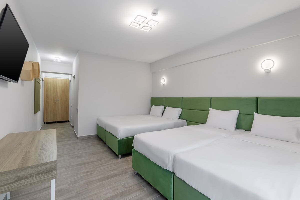 Habitación de hotel con dos camas individuales, un televisor de pantalla plana, un armario de madera y una pared de acento verde.