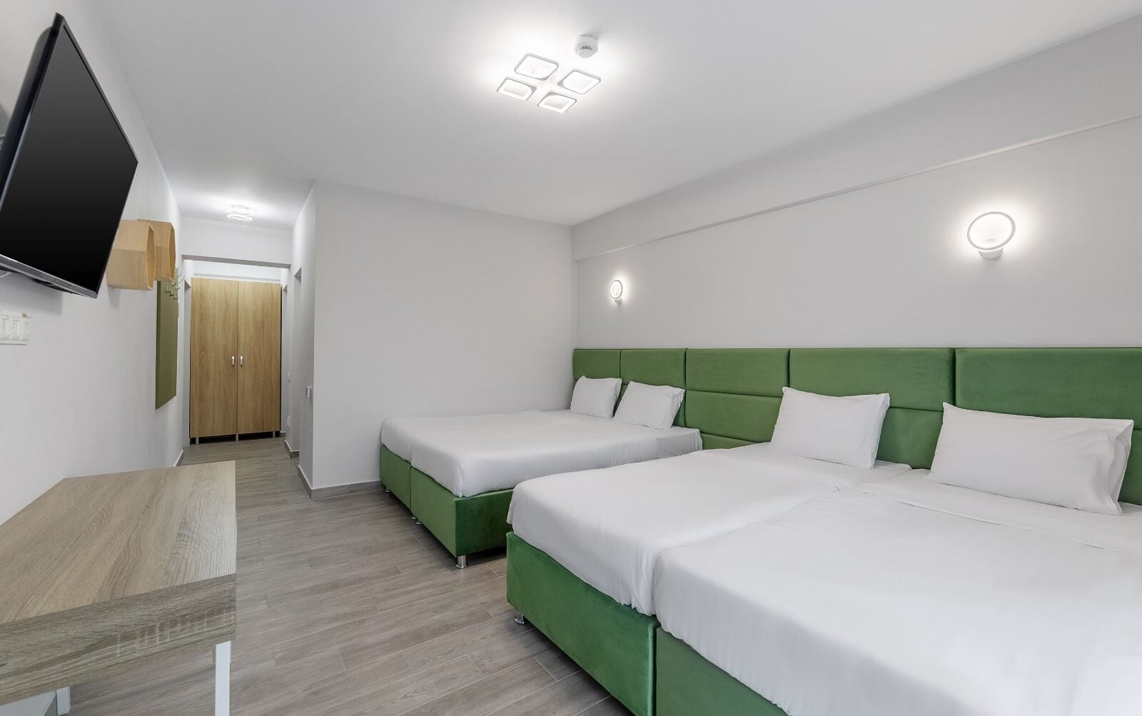 A hotel room with two single beds, a flat-screen TV, a wooden wardrobe, and a green accent wall.