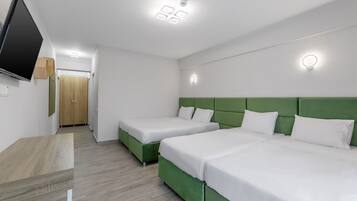 A hotel room with two single beds, a flat-screen TV, a wooden wardrobe, and a green accent wall.