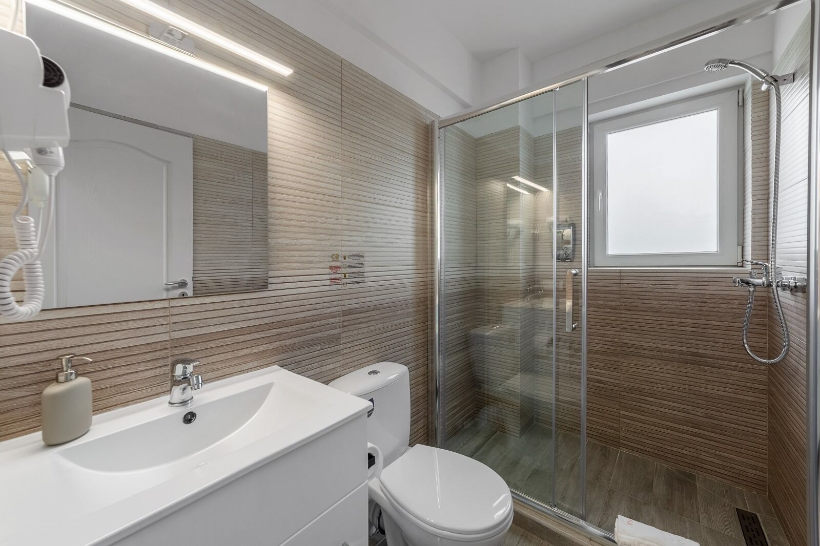 A modern bathroom with a glass-enclosed shower, a large mirror, and a white sink.