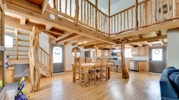 Ein geräumiger Wohnbereich mit einer Holztreppe, einem Esstisch mit Stühlen und einer Küche im Hintergrund.