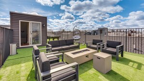 Une terrasse extérieure comprenant un ensemble de meubles de salon, un foyer et un petit bâtiment doté d’une porte coulissante.