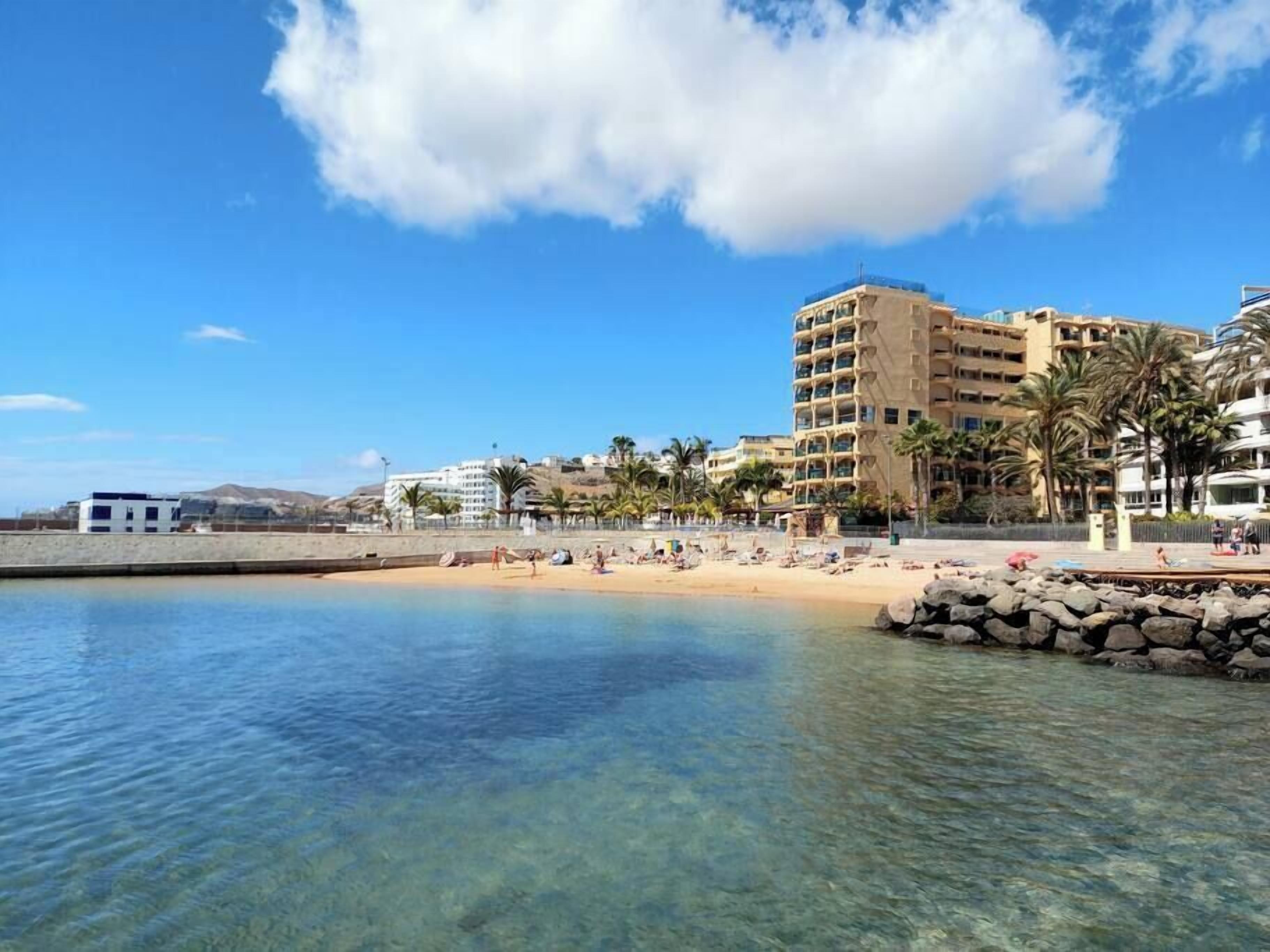 Un hotel frente a la playa con aguas azul cristalino, una playa de arena y palmeras.