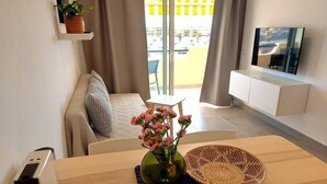 Ett modernt vardagsrum med en soffa, ett soffbord med en vas med blommor, en tv och en grenuttag.