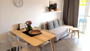 Ett modernt vardagsrum med en soffa, ett matbord med stolar, en klocka på väggen och ett fönster med gardiner.