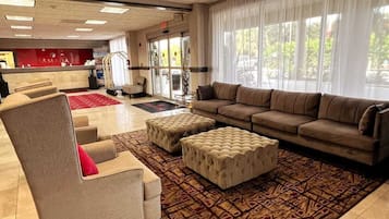 A spacious lobby with a reception desk, a sofa, ottomans, and a patterned rug.