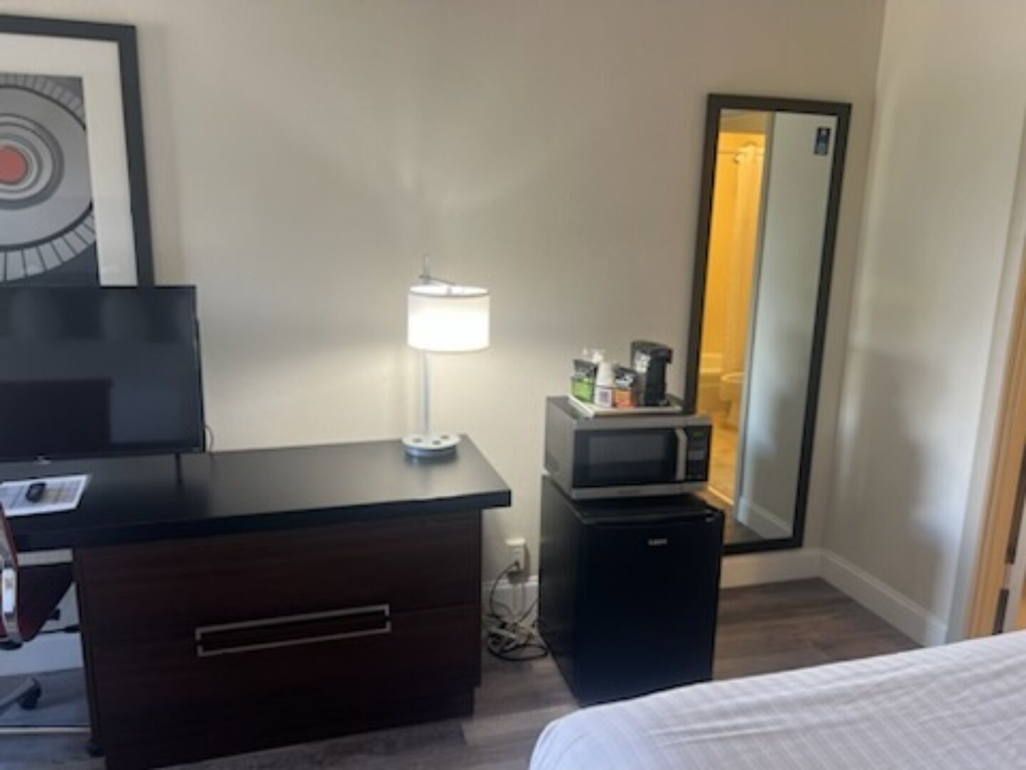 Ein Hotelzimmer mit einem Bett, einem Schreibtisch mit Lampe, einem Fernseher, einer Mikrowelle und einem kleinen Kühlschrank.