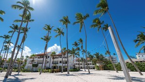 A beach with tall palm trees and a building with multiple balconies.
