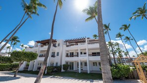 A multi-story hotel with a white facade, balconies, and palm trees in the foreground.