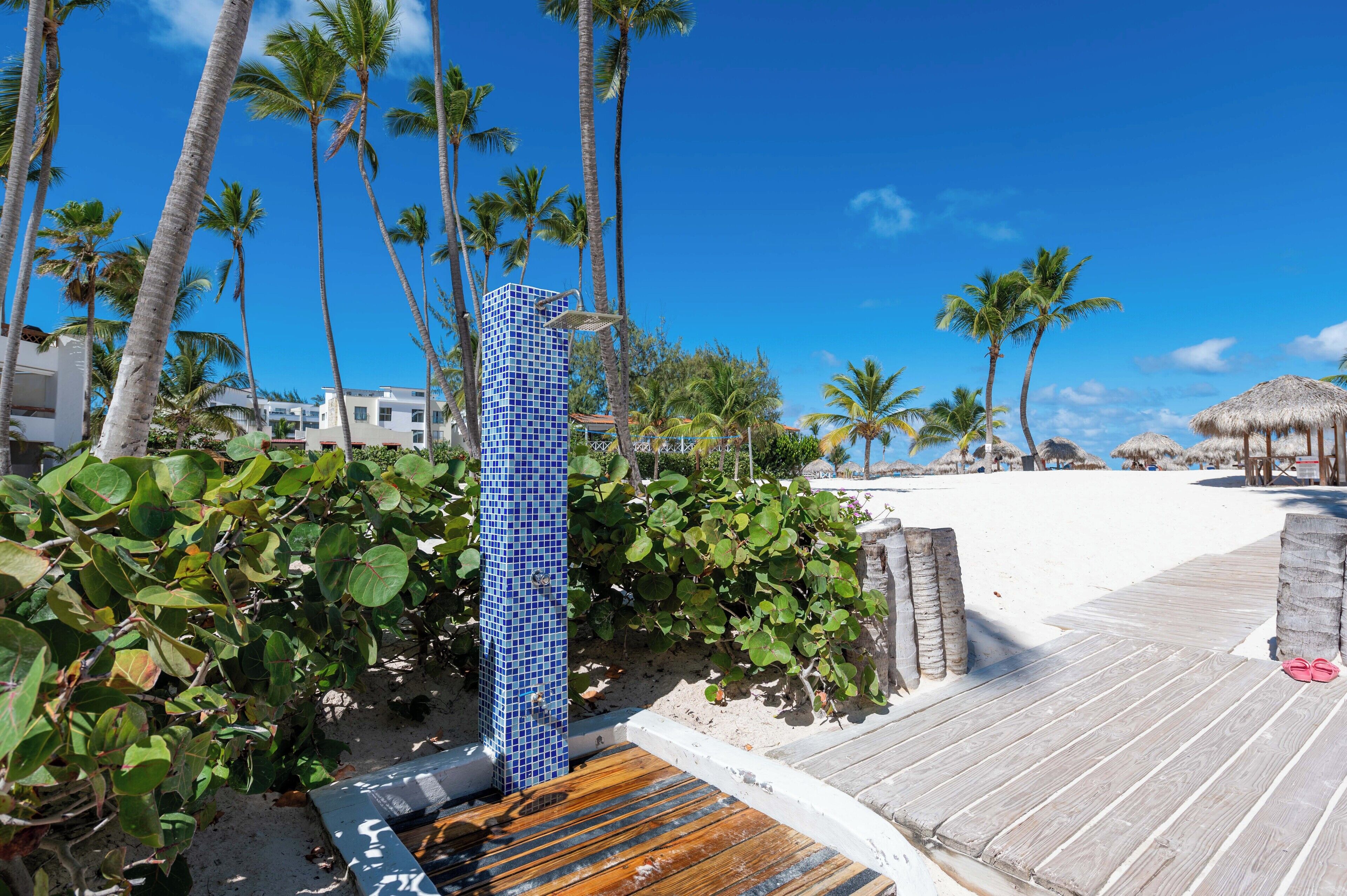 Una terraza de madera que da a una playa con palmeras y una estructura de azulejos azules.