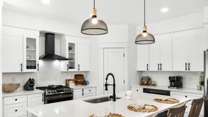 Cozinha moderna com armários brancos, ilha central com pia e iluminação pendente.