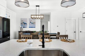 Una cocina moderna con un lavamanos de acero inoxidable, una mesa de comedor de madera y luces colgantes.
