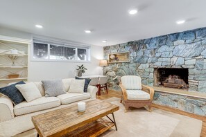 A living room with a stone wall fireplace, a white sofa, a wicker armchair, and a wooden coffee table. - Commuter-Friendly Seattle Apartment! Dogs Welcome (Seattle)