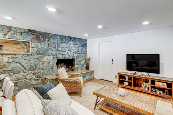 A living room with a stone wall, a fireplace, a television, and a sofa. - Commuter-Friendly Seattle Apartment! Dogs Welcome (Seattle)
