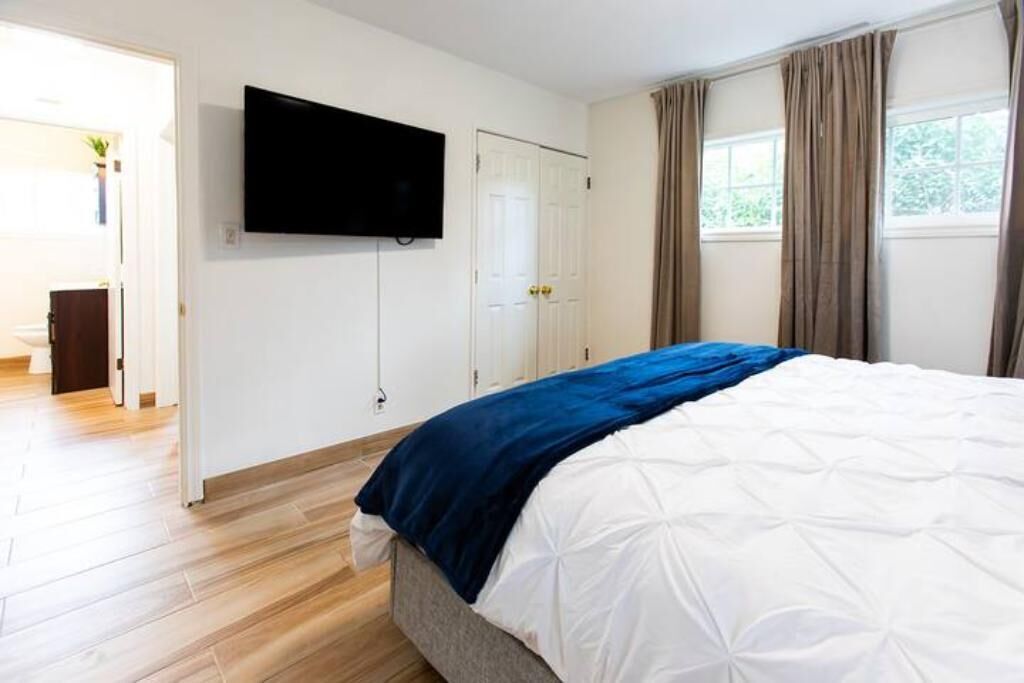 A bedroom with a bed, a TV mounted on the wall, a door, and a window with curtains.