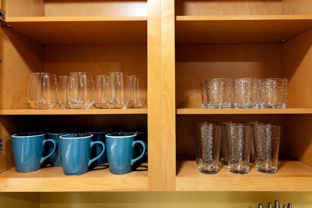 A wooden shelf unit with clear glasses, blue mugs, and textured glassware.