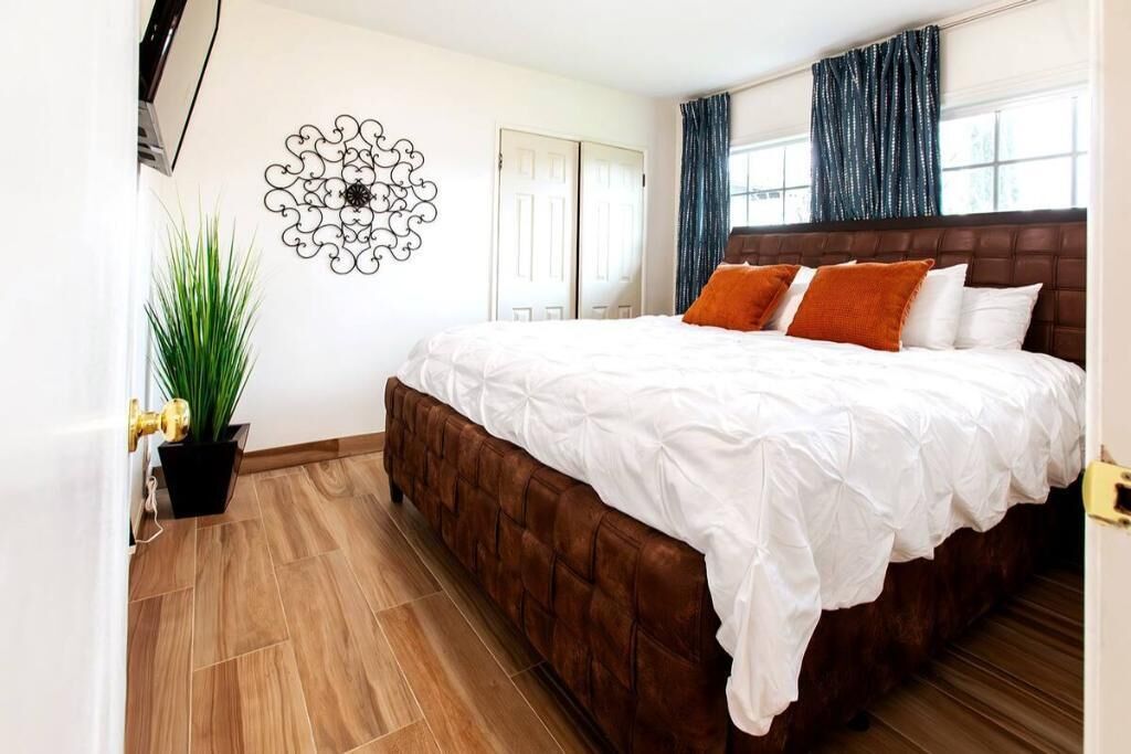 A bedroom with a large bed, a potted plant, a decorative wall piece, and a door.