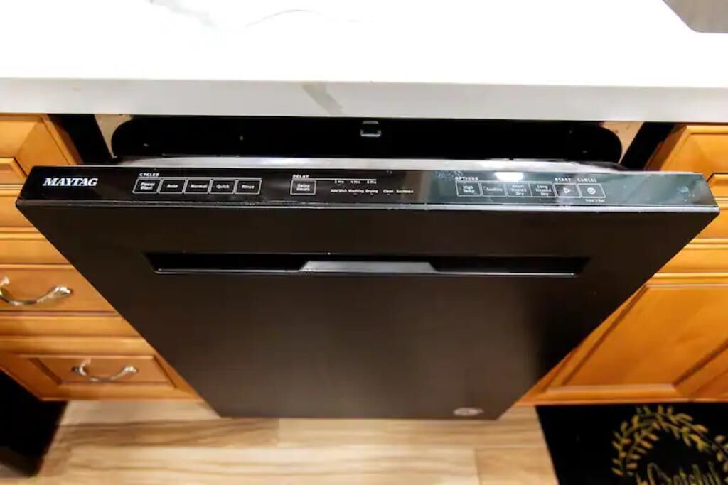 A black Maytag dishwasher installed under a kitchen counter with wooden cabinets.