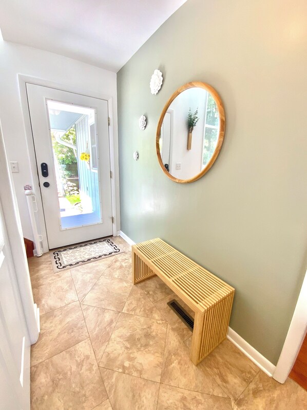 A hallway with a bench, a round mirror, and a door leading outside.