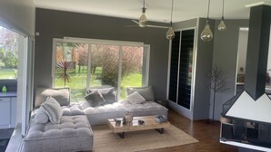 A modern living room with a grey sofa set, a wooden coffee table, and a large window offering a view of a garden. - Villa 290m2, Piano, Piscine et Spa, Parc Arboré Entre Bordeaux et St Emilion (Sallebœuf)